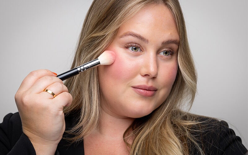 Blush wird mit einem Pinsel auf die Wangen aufgetragen